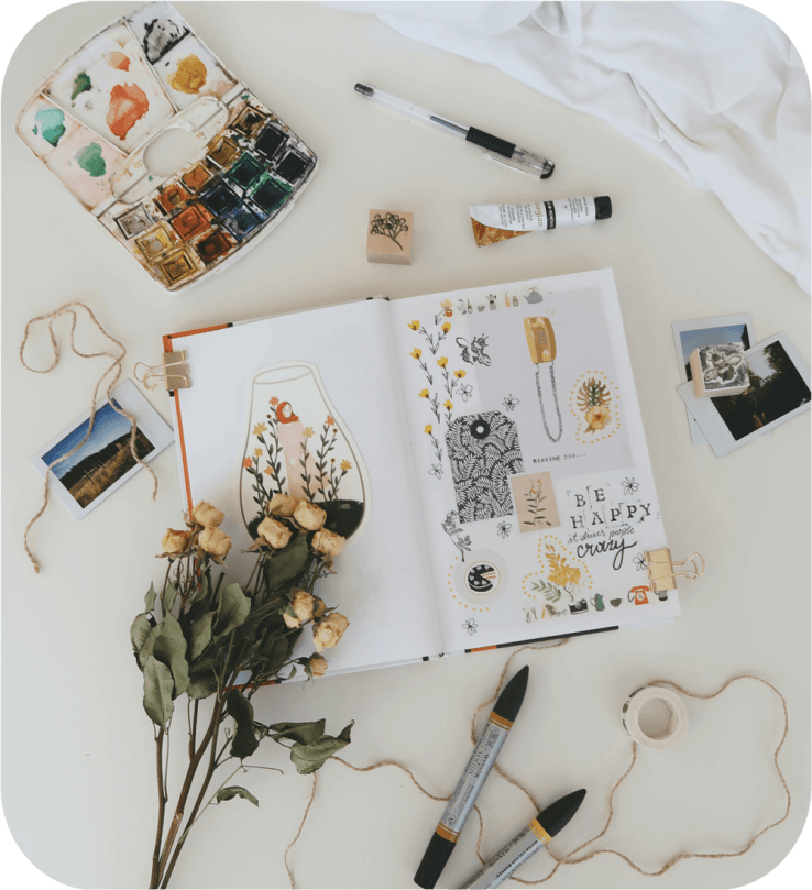 journal, art supplies, and some flowers on a white desk